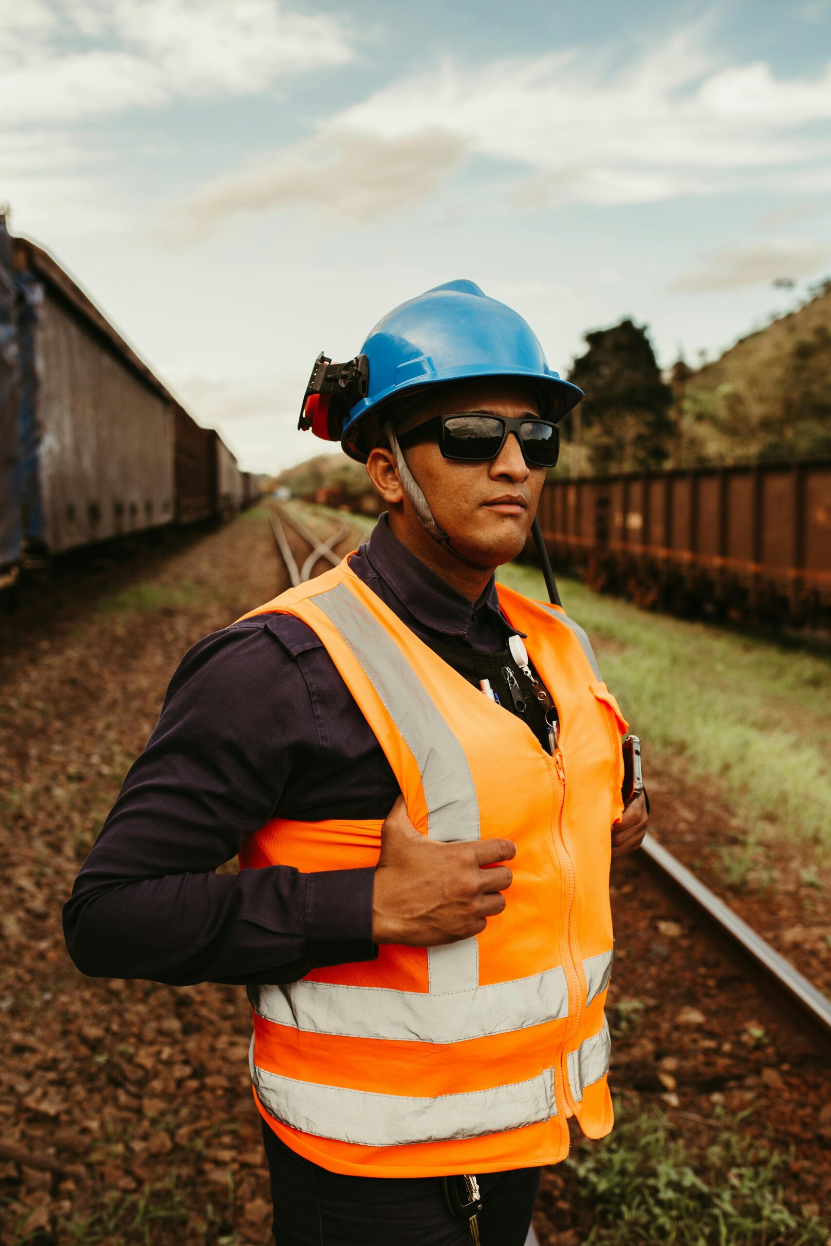 Confident railway worker wearing safety vest and helmet on tracks outdoors.